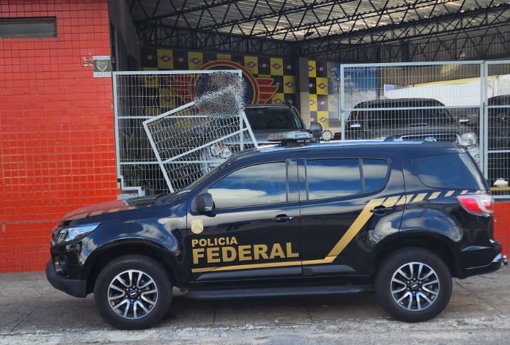 Imagem de viatura da Polícia Federal em frente a loja de veículos.