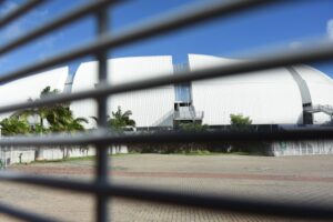 Fotografia do estádio Arena das Dunas, mostrando o gradeado em primeiro plano e o estádio em segundo plano.