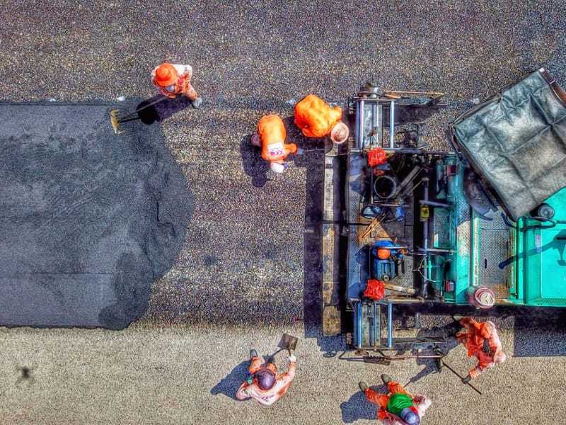 Imagem aérea de trabalhadores realizando serviços de pavimentação.