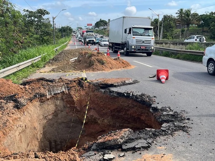 Imagem do buraco aberto no asfalto com veículos utilizando uma via da BR.