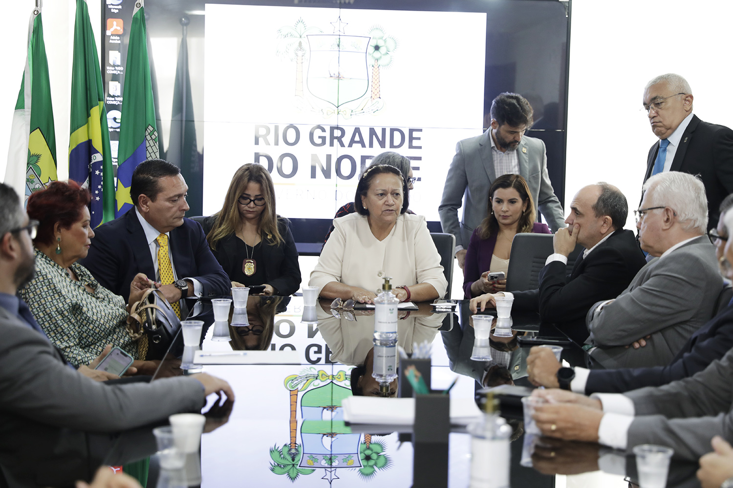 Governadora e autoridades sentadas à mesa em reunião de emergência no combate aos ataques criminosos.