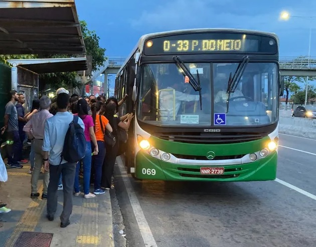 Passageiros na parada de ônibus e outros embarcando em veículo.